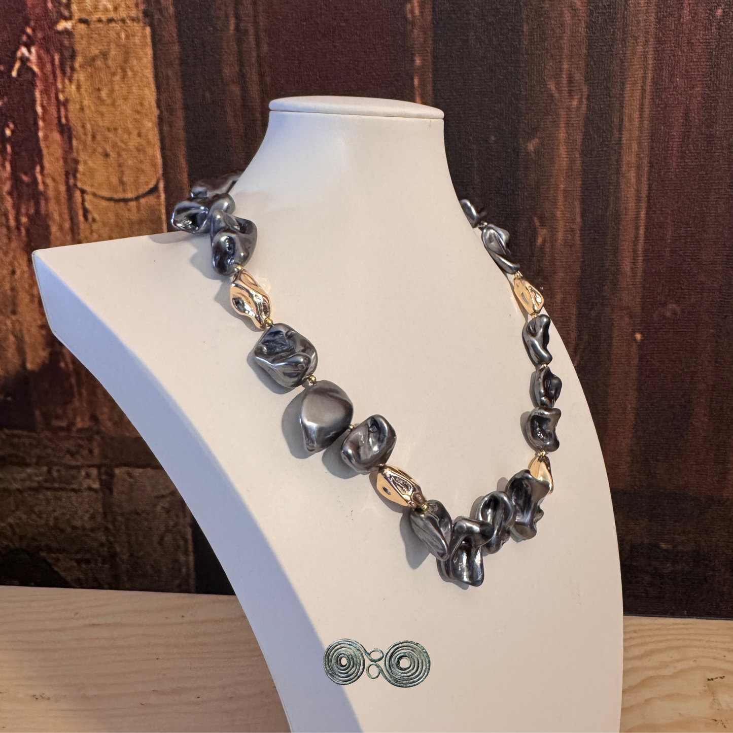 Dettaglio perle di conchiglia irregolari grigio scuro con riflessi metallici e perle oro.