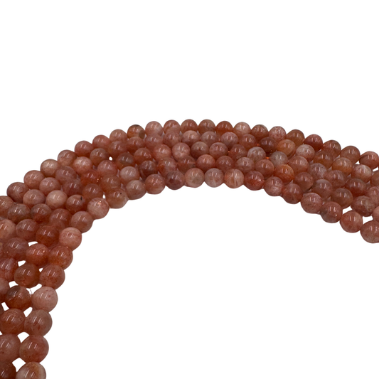 Primo piano del filo di Pietra del Sole, perle tonde lisce 6 mm, che mostrano il colore arancione e i riflessi dorati.