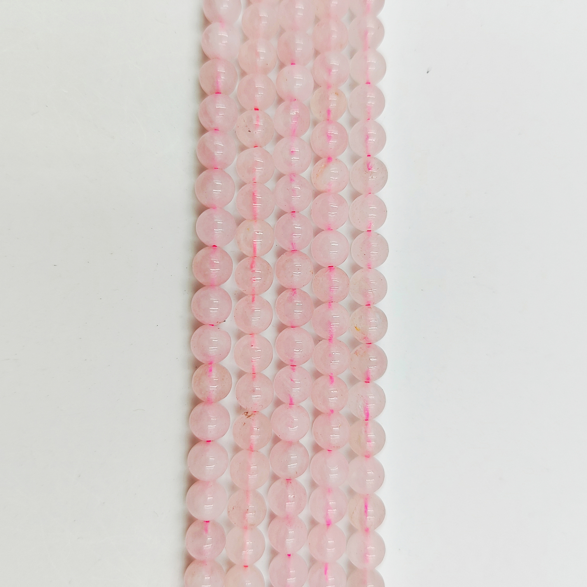 Primo piano del filo di Quarzo Rosa 6mm, che mostra il colore rosa pallido e la finitura liscia.