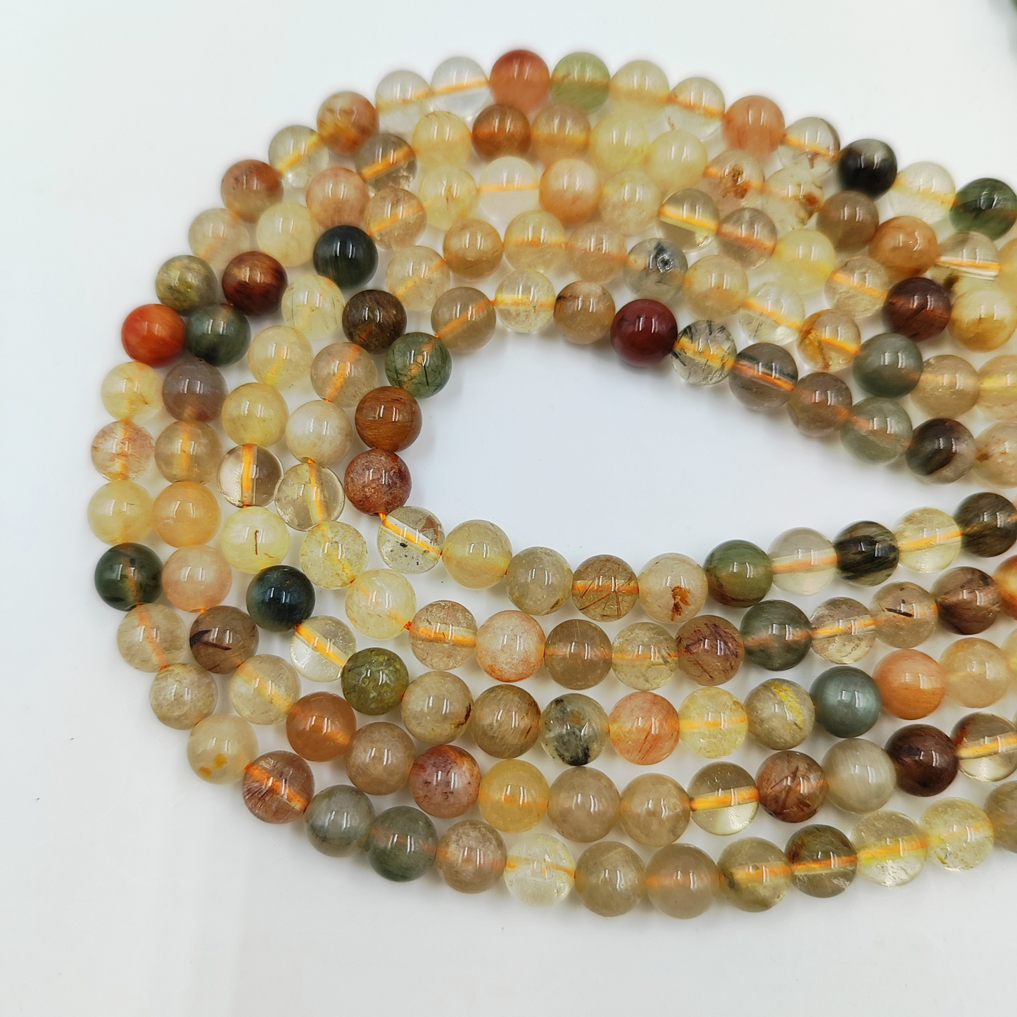 Primo piano del filo di Quarzo Rutilato Arcobaleno, perle lisce 6 mm, che mostrano le inclusioni e i riflessi colorati.