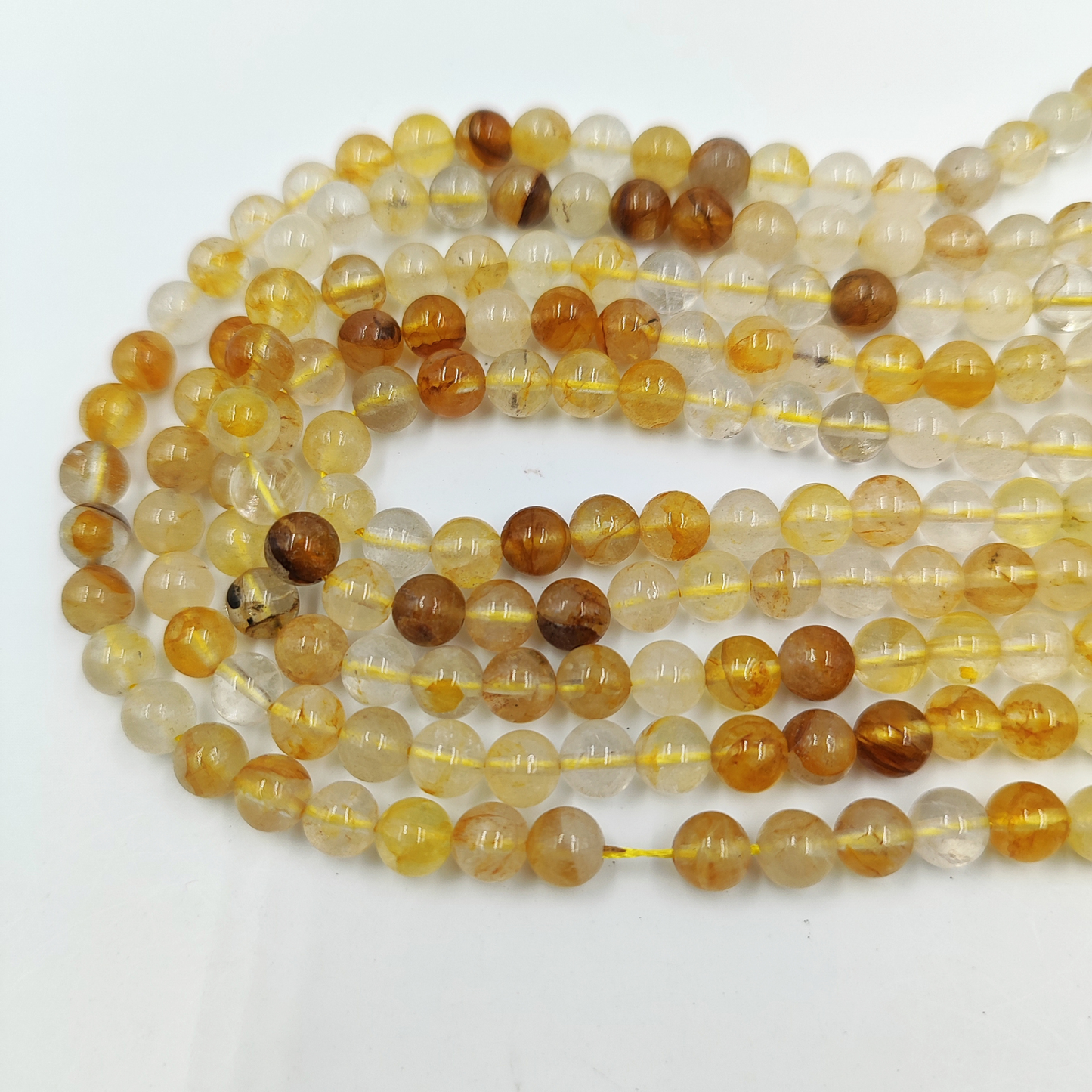 Primo piano del filo di Quarzo di Limonite 6mm, che mostra le inclusioni arancio/rosse nella matrice trasparente.