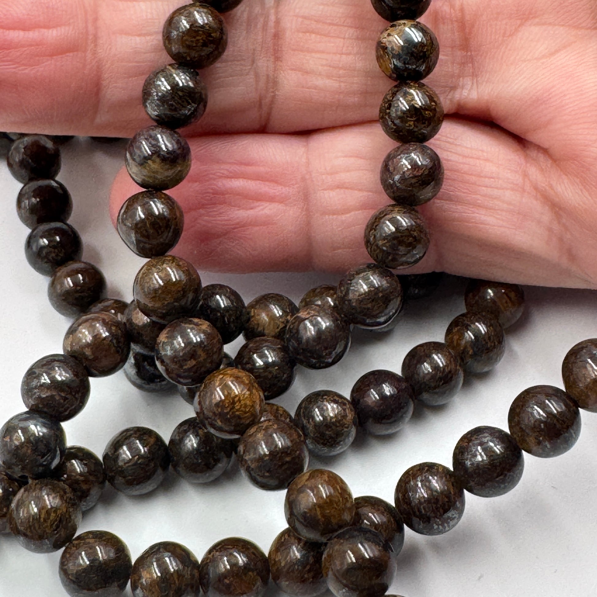 Filo di perle sferiche lisce di Bronzite naturale da 6 mm, con tonalità marrone scuro e riflessi metallici color bronzo.