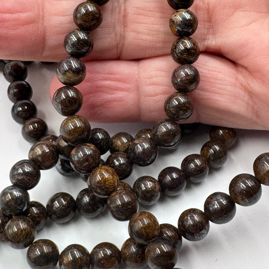 Filo di perle sferiche lisce di Bronzite naturale da 6 mm, con tonalità marrone scuro e riflessi metallici color bronzo.