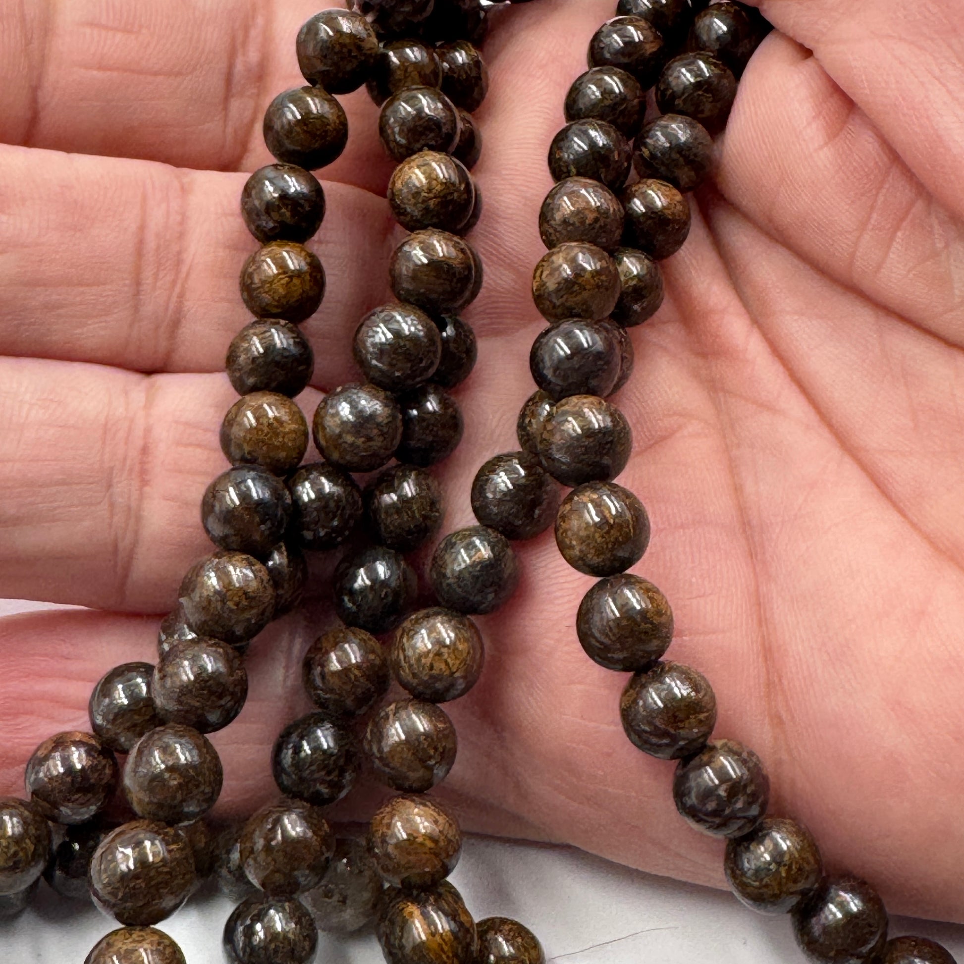 Dettaglio ravvicinato delle perle in Bronzite (PE0961-06) di 6 mm, che evidenzia l'effetto bronzite e la finitura lucida.